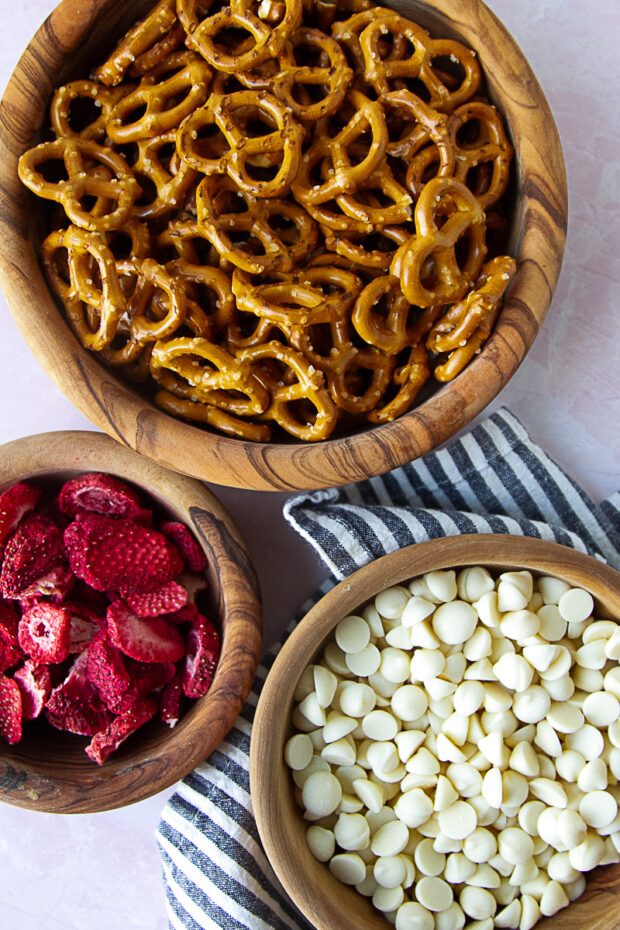 Ingredients for strawberry white chocolate pretzels in wooden bowls -- pretzel twists, white chocolate chips, freeze-dried strawberries.