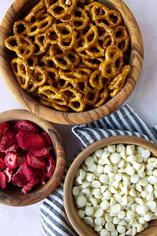 Ingredients for strawberry white chocolate pretzels in wooden bowls -- pretzel twists, white chocolate chips, freeze-dried strawberries.