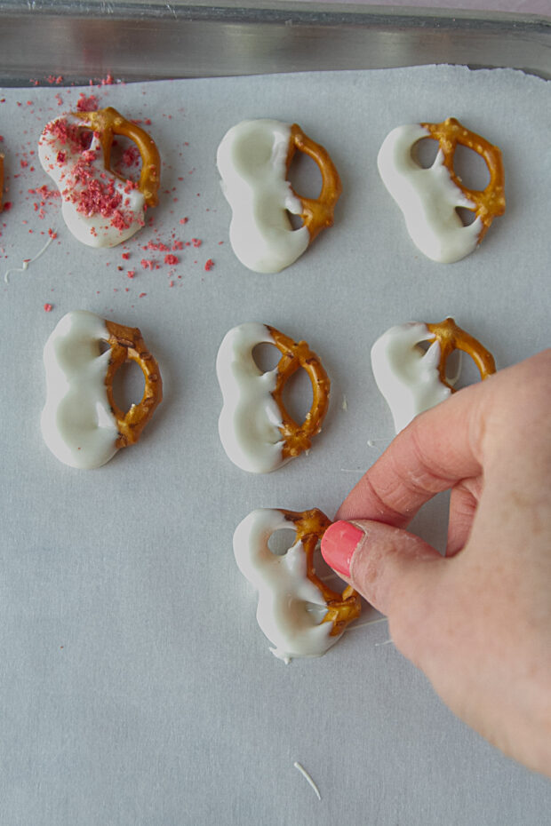 Freshly dipped white chocolate pretzels laid on parchment paper.