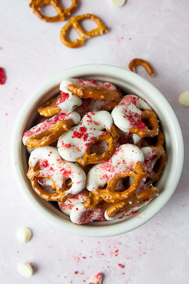 White bowl with pretzel twist half dipped in white chocolate and sprinkled with freeze-dried strawberries.