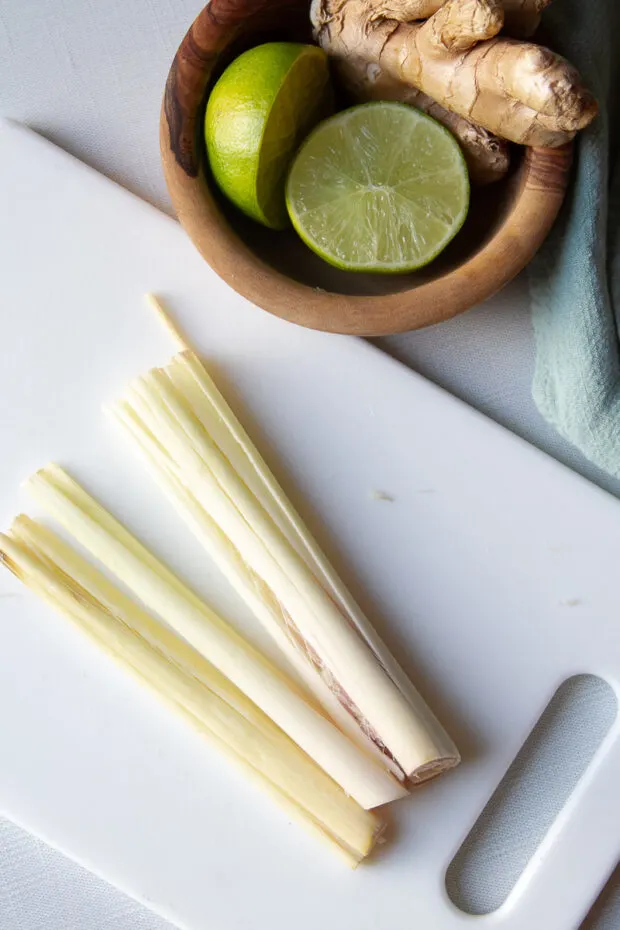 Two lemongrass stalks on a cutting board that have been smashed with the back of a knife.