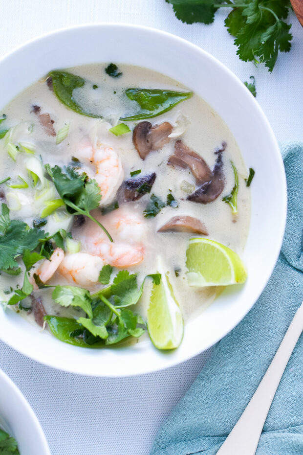 Bowl of Thai coconut soup garnished with lime wedges and fresh cilantro.