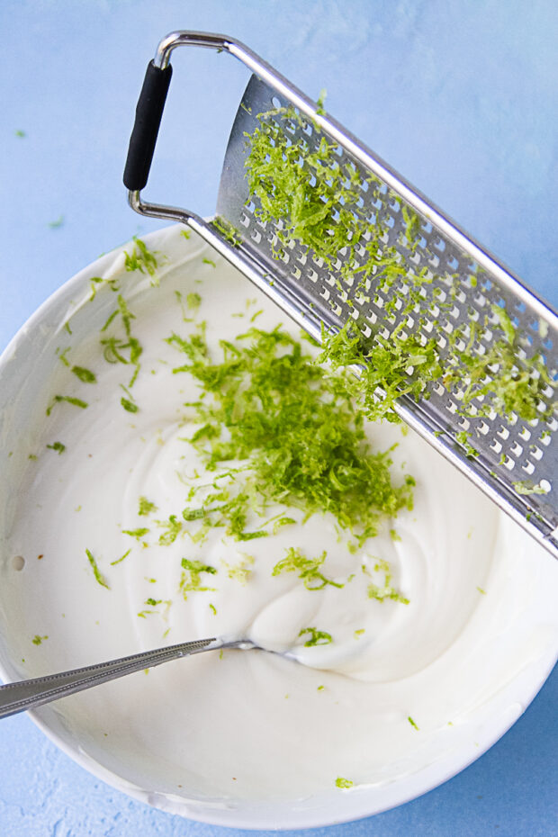 Lime zest being added to a bowl of melted white chocolate.