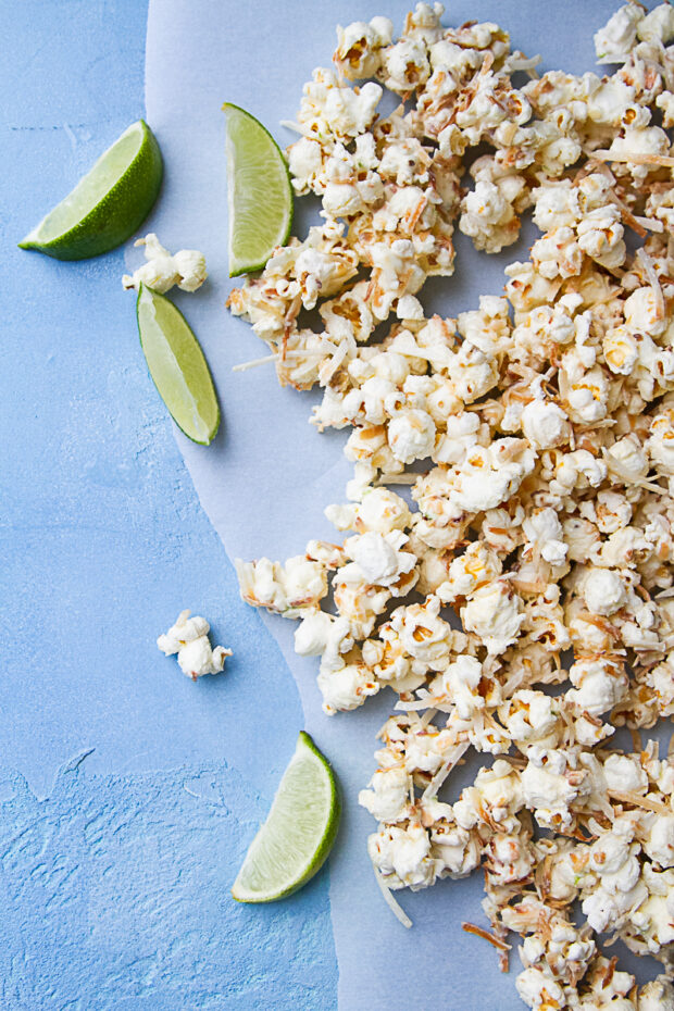 Finished toasted coconut popcorn spread out on some parchment paper with lime wedges.