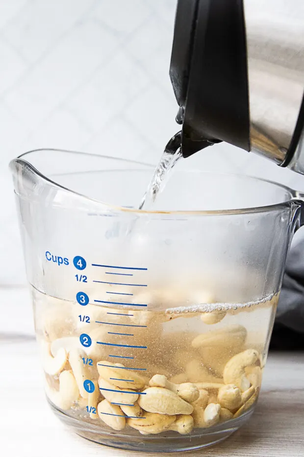 Boiling water from a kettle poured into a large glass measuring cup with cashews.
