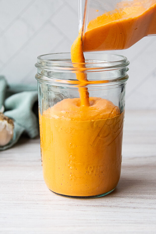 Finished vegan roasted red pepper sauce poured from a blender to a glass canning jar.