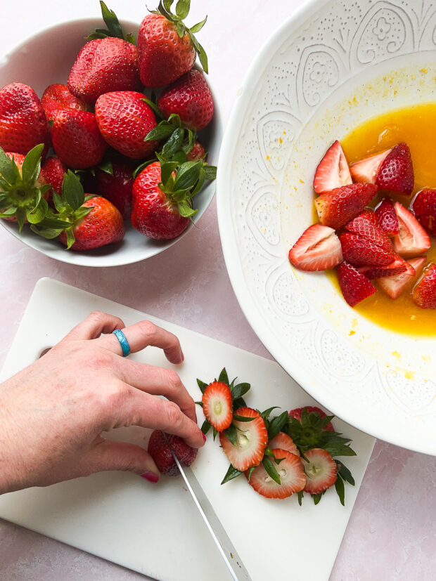 Action shot of berries being trimmed and placed into the serving bowl with the dressing.