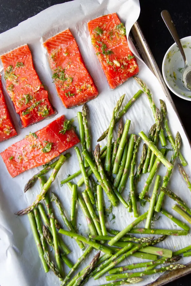 Salmon and asparagus on a sheet pan covered in the herb-garlic-zest spread.