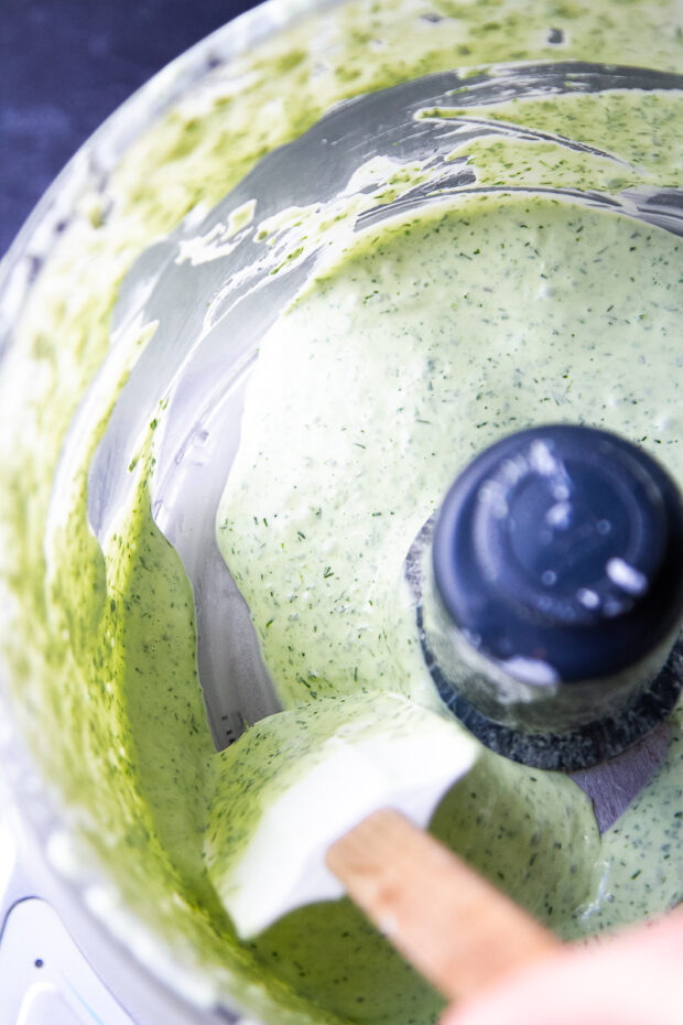 green goddess dip in the work bowl of a food processor after it has blended.