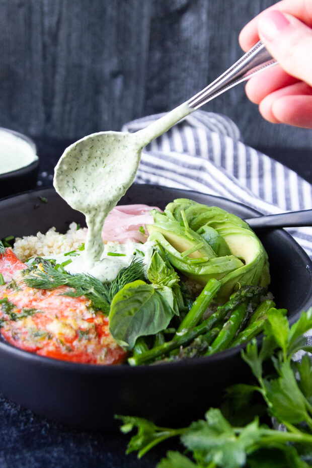 Green Goddess dip added to a bowl filled with roasted salmon, asparagus, avocado, fresh herbs, and quinoa.