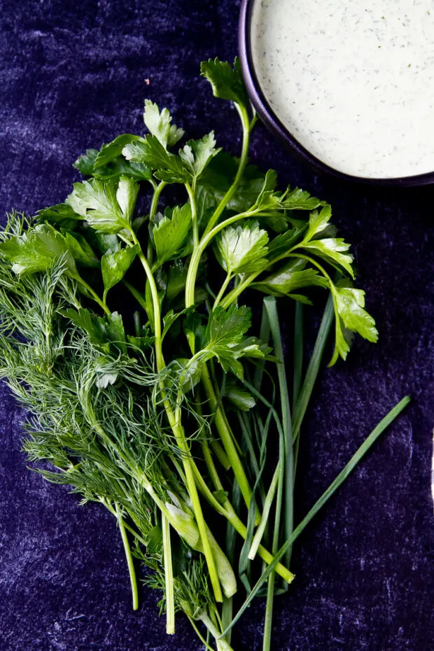 Fresh parsley, dill, and chives next to a bowl of green goddess dip.