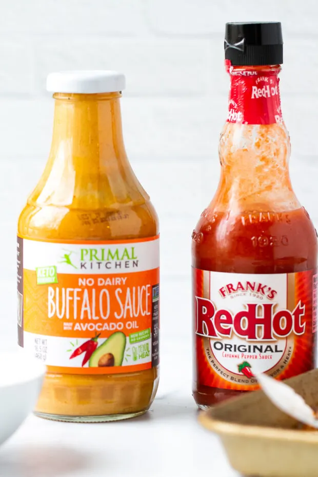 A bottle of Primal Kitchen Buffalo Sauce and Franks Hot Sauce.
