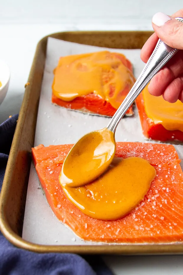 Spreading buffalo sauce on uncooked salmon fillets.