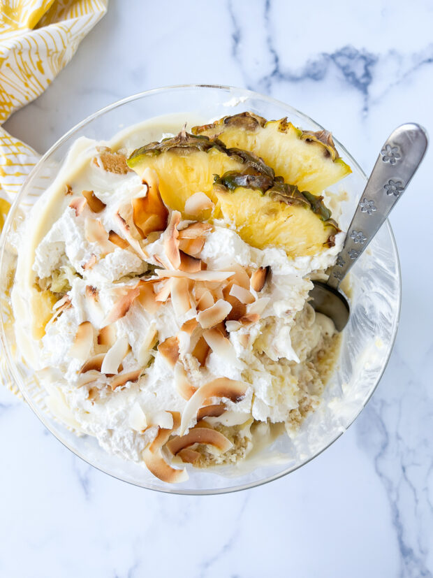 Overhead shot of the coconut trifle garnished with lots of whipped cream, pineapple wedges and toasted coconut chips.