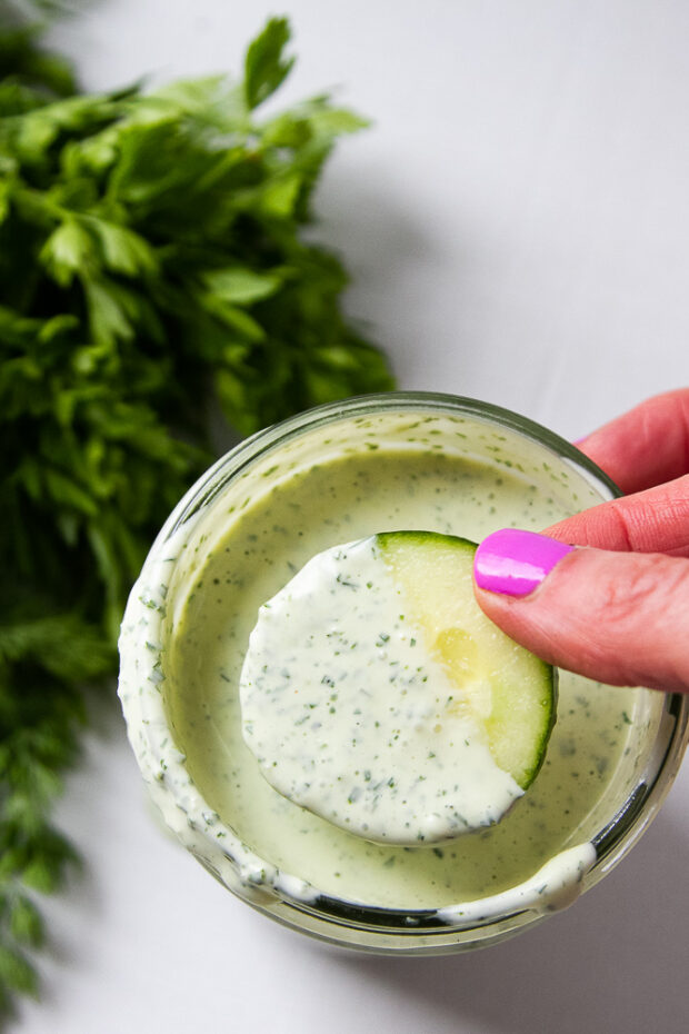 Green goddess dip in a mason jar showing a cucumber sliced dipped halfway.