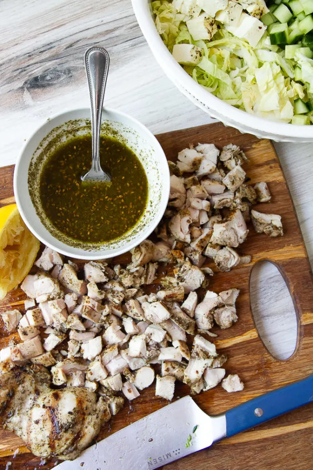 Grilled chicken chopped on a cutting board with a small bowl of dressing.