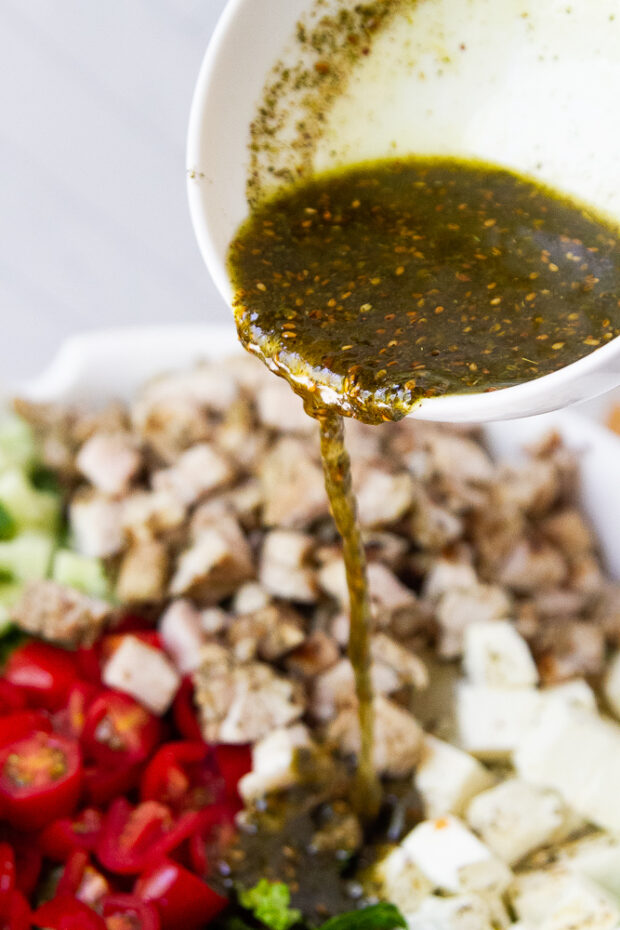 Pouring dressing over the grilled chicken salad.
