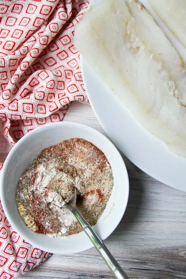 Bowl of blackening spice mix next to a plate with a raw cod fillet.