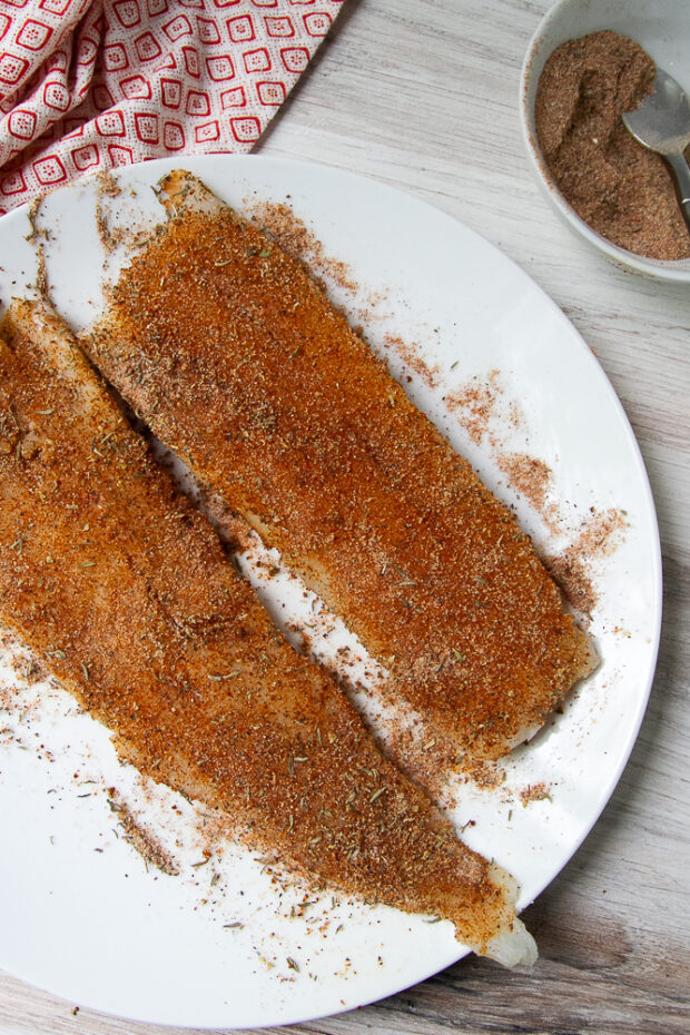 Two raw cod fillets that have been coated in the blackening seasoning.