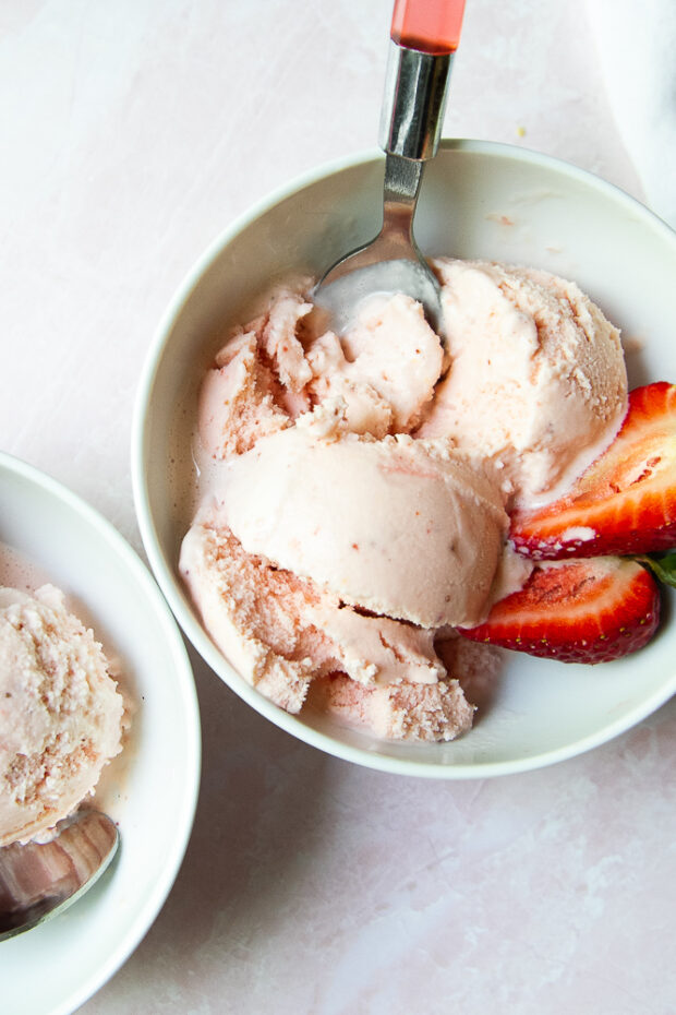 Bowl of strawberry frozen Greek yogurt with fresh strawberries on the side.