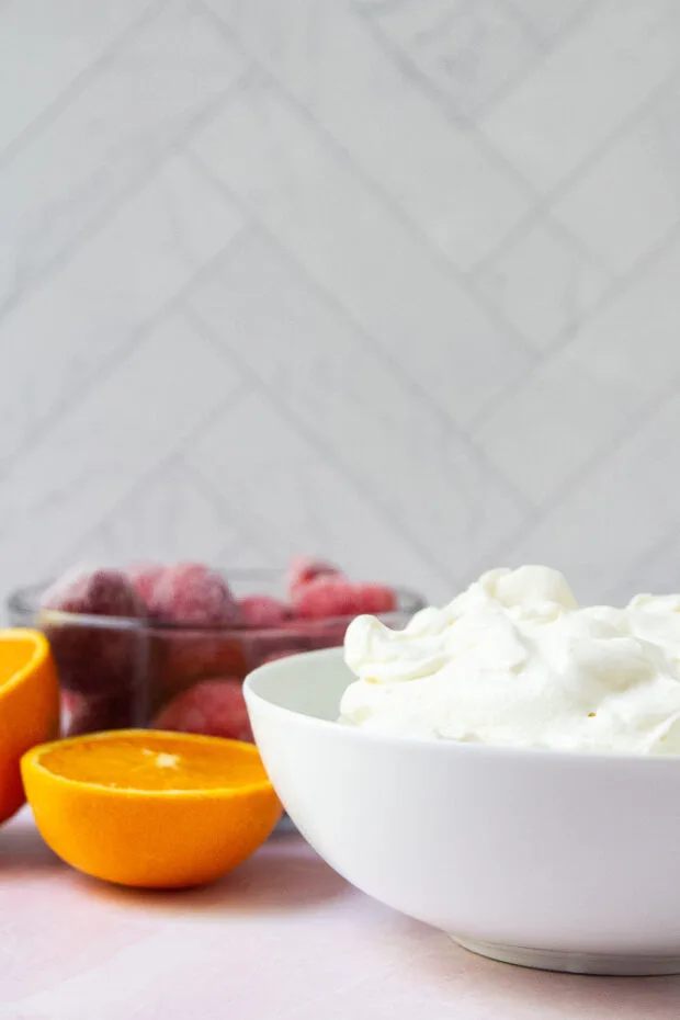 Bowl of Greek yogurt, bowl of frozen strawberries and an orange cut in half.