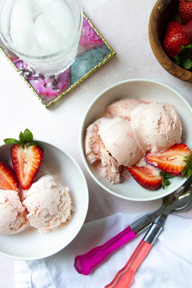 Bowls of strawberry frozen Greek yogurt with freshly sliced strawberries on the side.
