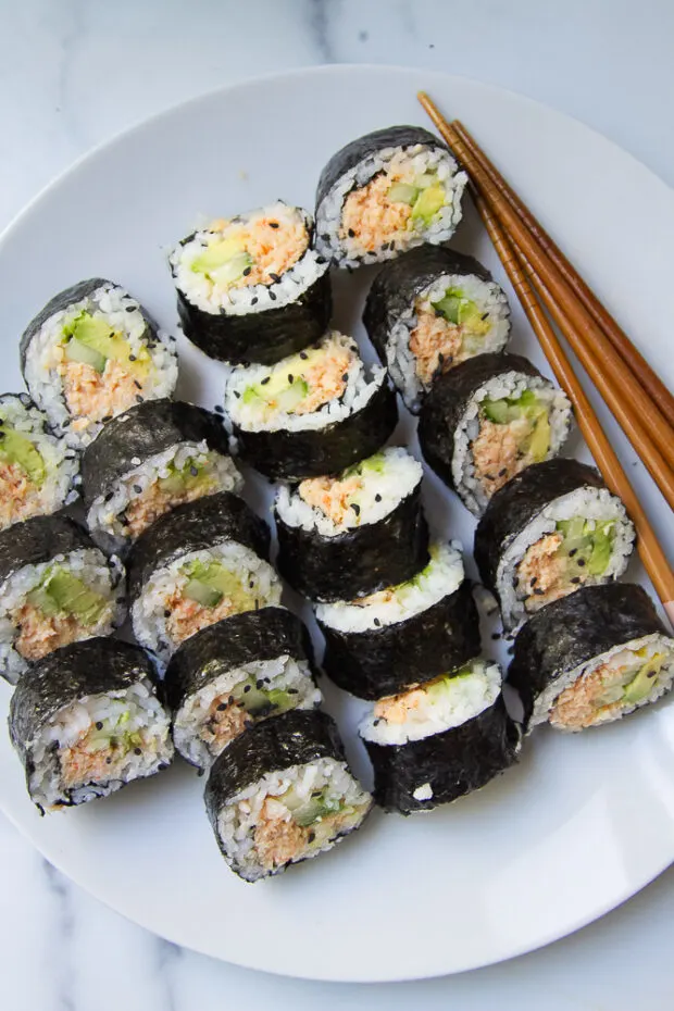 A plate full of spicy shrimp roll pieces with some chopsticks alongside.