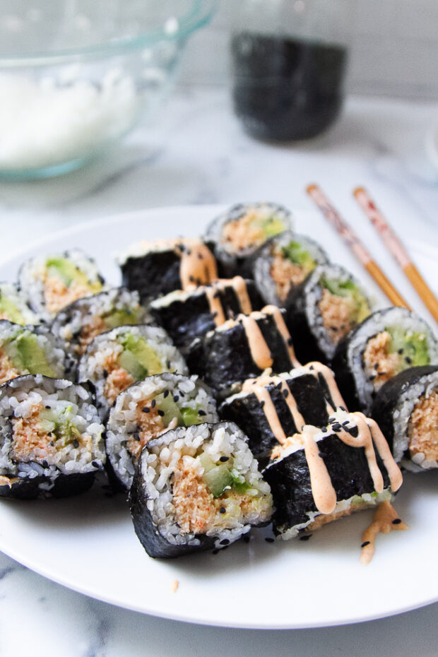 A plate of sliced spicy shrimp rolls garnished with a drizzle of sriracha mayo.