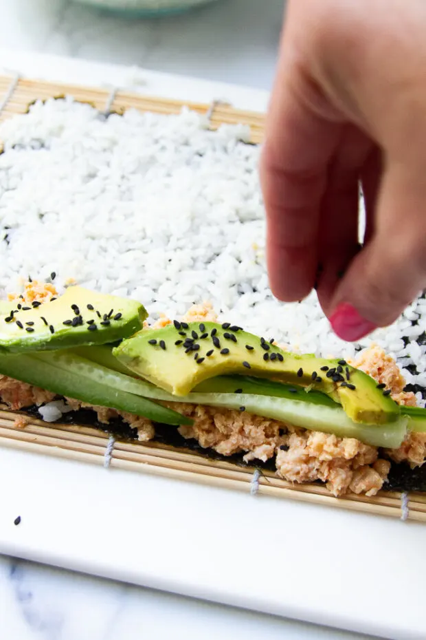 Spicy shrimp, cucumber, and avocado has been added to the blank part of the nori wrapper with a sprinkle of black sesame seeds.