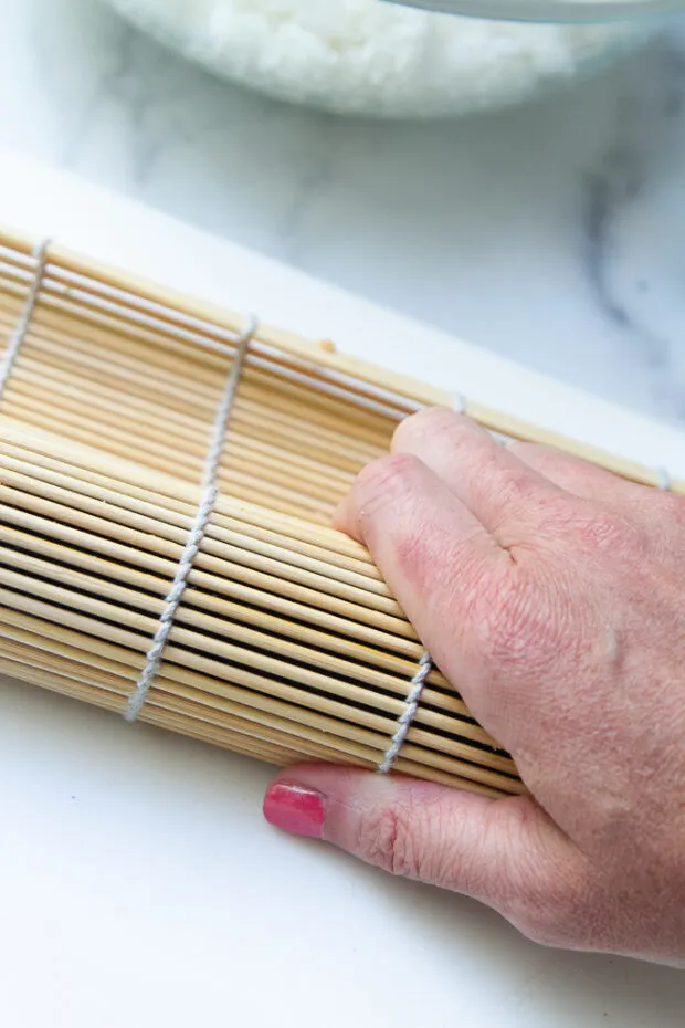 Rolled up sushi roll being pressed tighter using the bamboo mat.