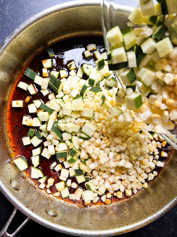 Adding the fresh corn and zucchini to the skillet with the seasoned oil.