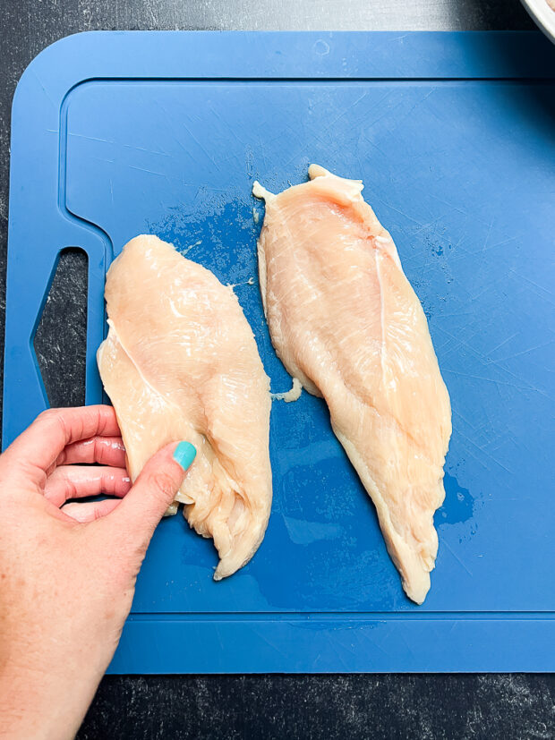 Two thin chicken cutlets on a cutting board.