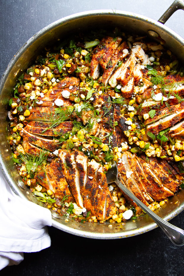 A skillet with sliced blackened chicken and sautéed corn and zucchini.