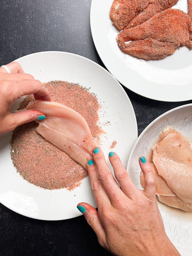 Coating the chicken cutlets in blackening spices.