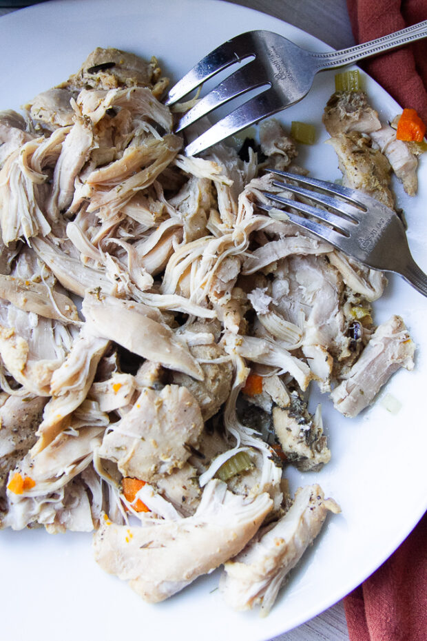 Cooked chicken thighs shredded with two forks.