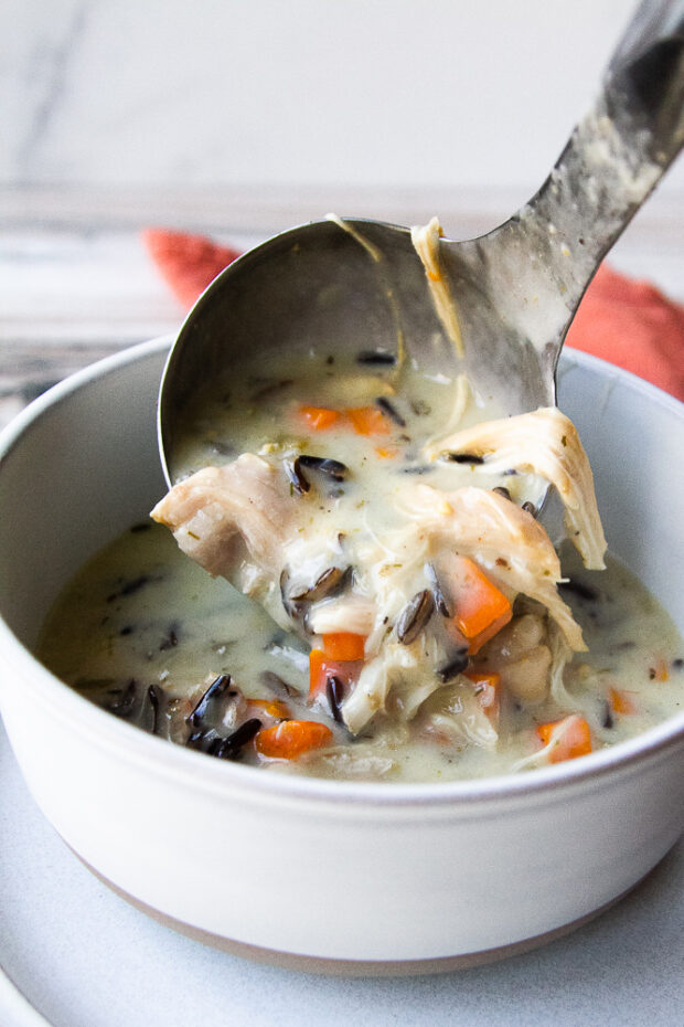 A ladle of wild rice and chicken soup transferred to a gray bowl.