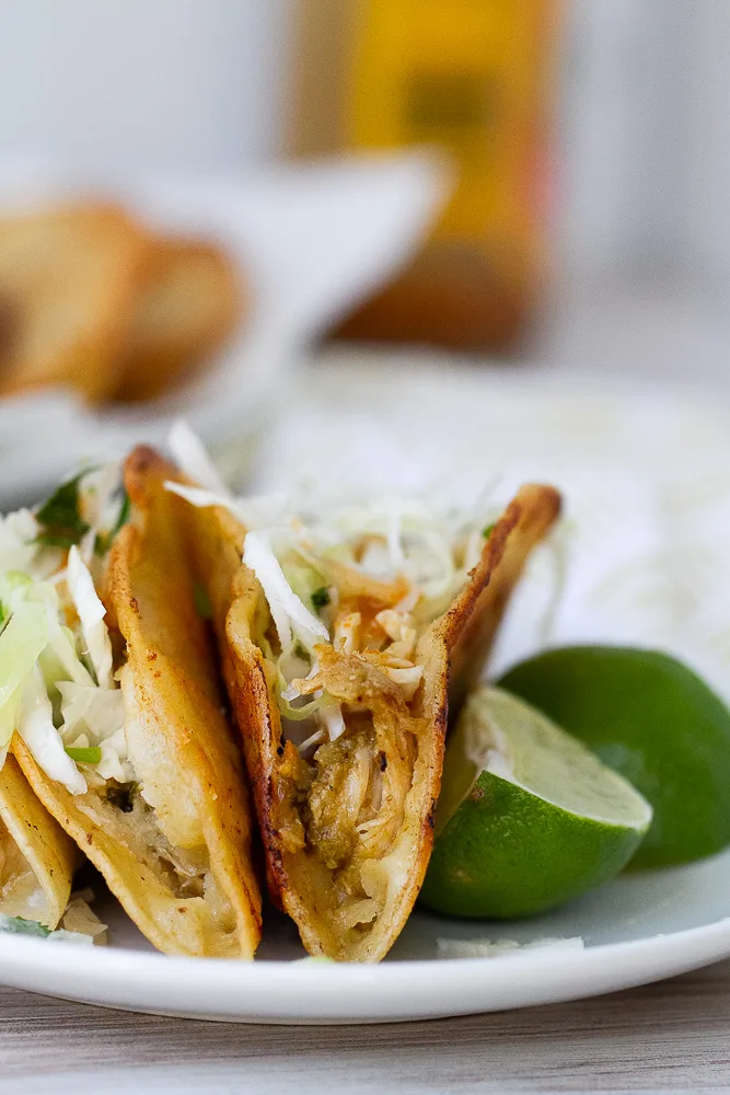 Crispy chicken tacos with lime wedges on a plate.