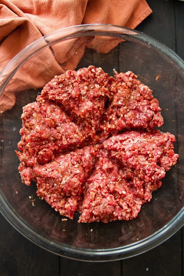 Ground beef in bowl that has lines created by pressing fingers into the meat in order to divide it into even sections for making patties.