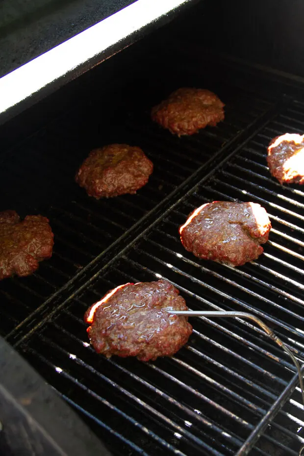 Burger patties on the grill with a meat thermometer inserted into one.