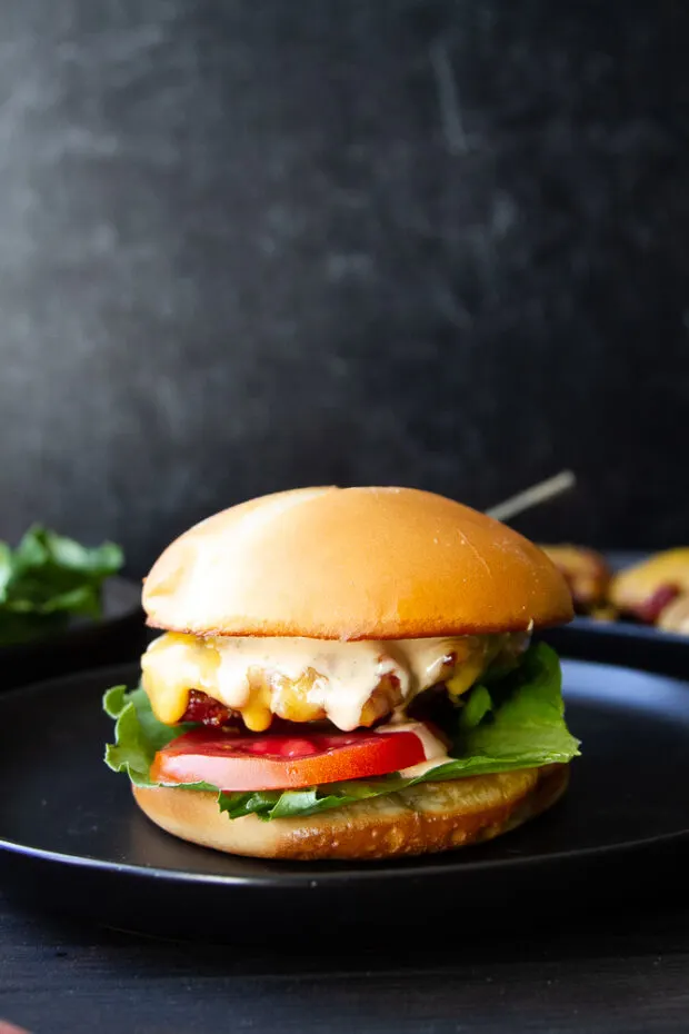 Finished smoked cheeseburger on a bun with dripping burger sauce, lettuce, and tomato.