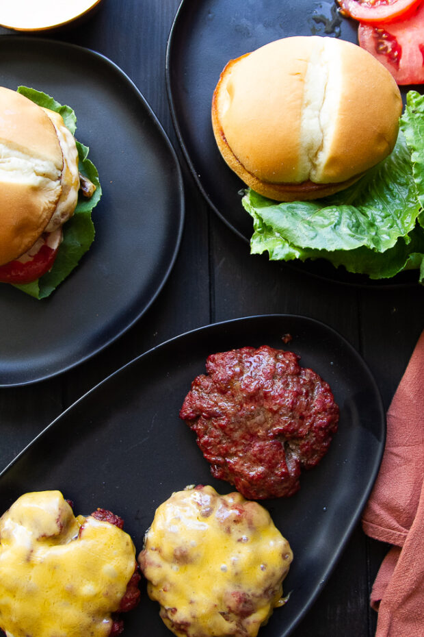 Overhead shot of finished burgers on a platter (some with cheese) and some burgers already assembled.