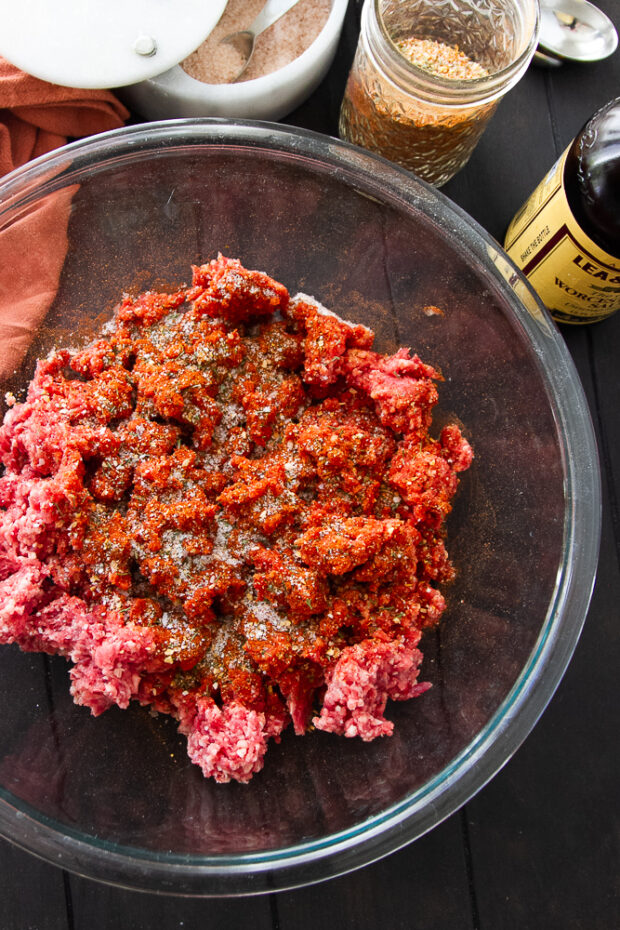 Clear bowl with ground beef. Steak seasoning and Worcestershire have been added.