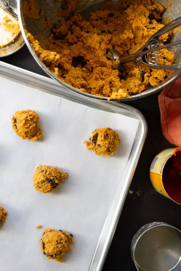 Pumpkin cookie dough balls on a parchment lined cookie sheet.