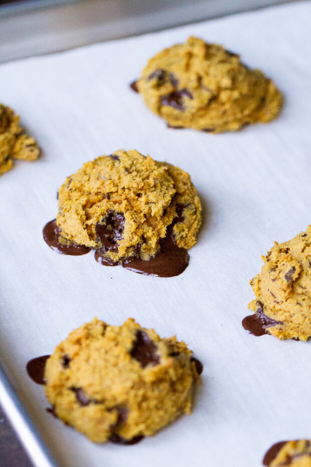 Close up of a freshly baked GF pumpkin cookie on the parchment with the dark chocolate oozing out a little. 