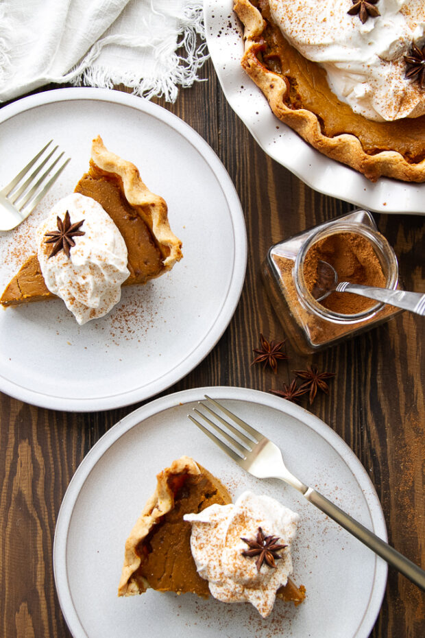 A couple pieces of pumpkin pie on plates garnished with whipped cream and star anise pods.