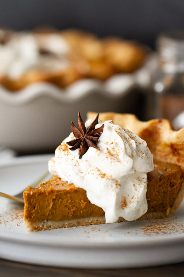 Slice of gluten free pumpkin pie topped with whipped cream on a plate.