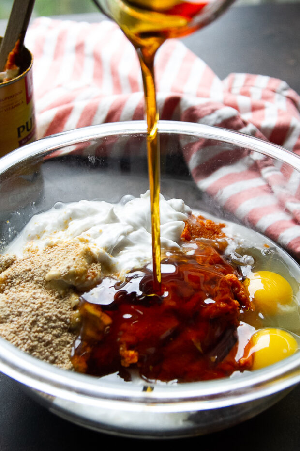 Maple syrup added to a glass bowl with the rest of the pumpkin pie filling ingredients.