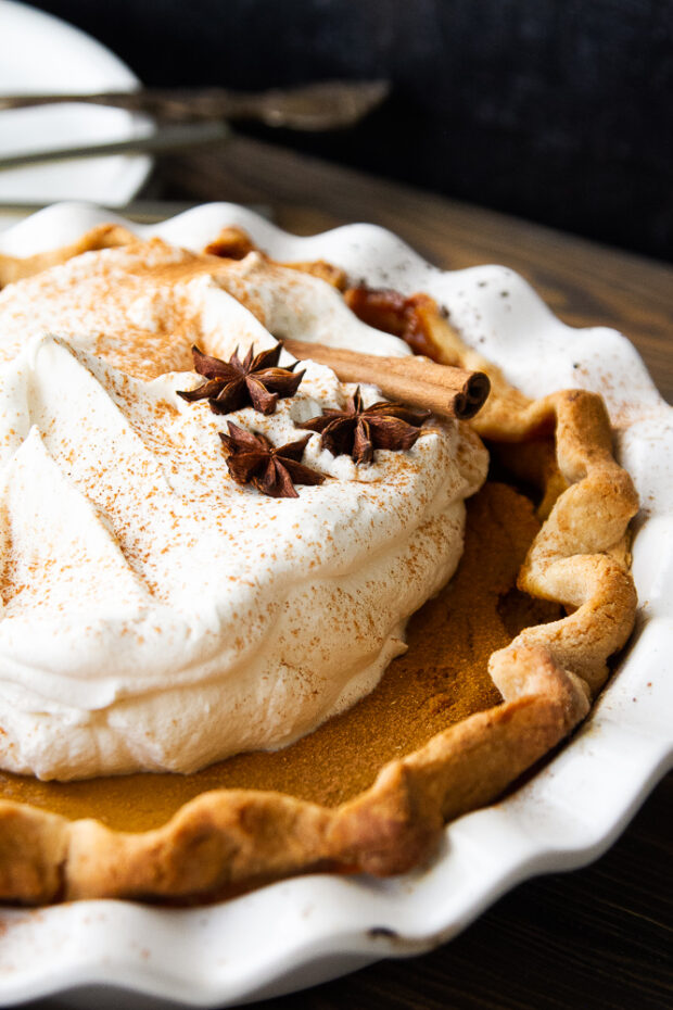 Another view of the finished pie with whipped cream, star anise pods, cinnamon sticks, and a dusting of cinnamon.