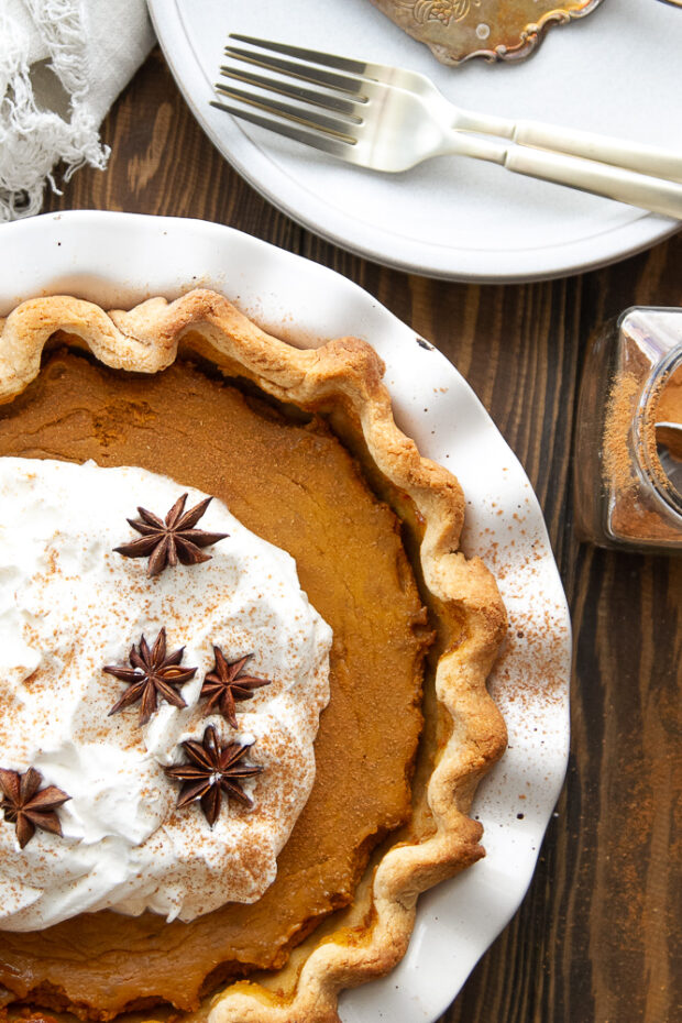View of the finished pie with a pile of whipped cream garnished with a few star anise pods and a dusting of cinnamon.