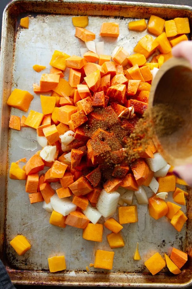 Large rimmed baking sheet with cubed vegetables piled in the center and spices sprinkled on top.